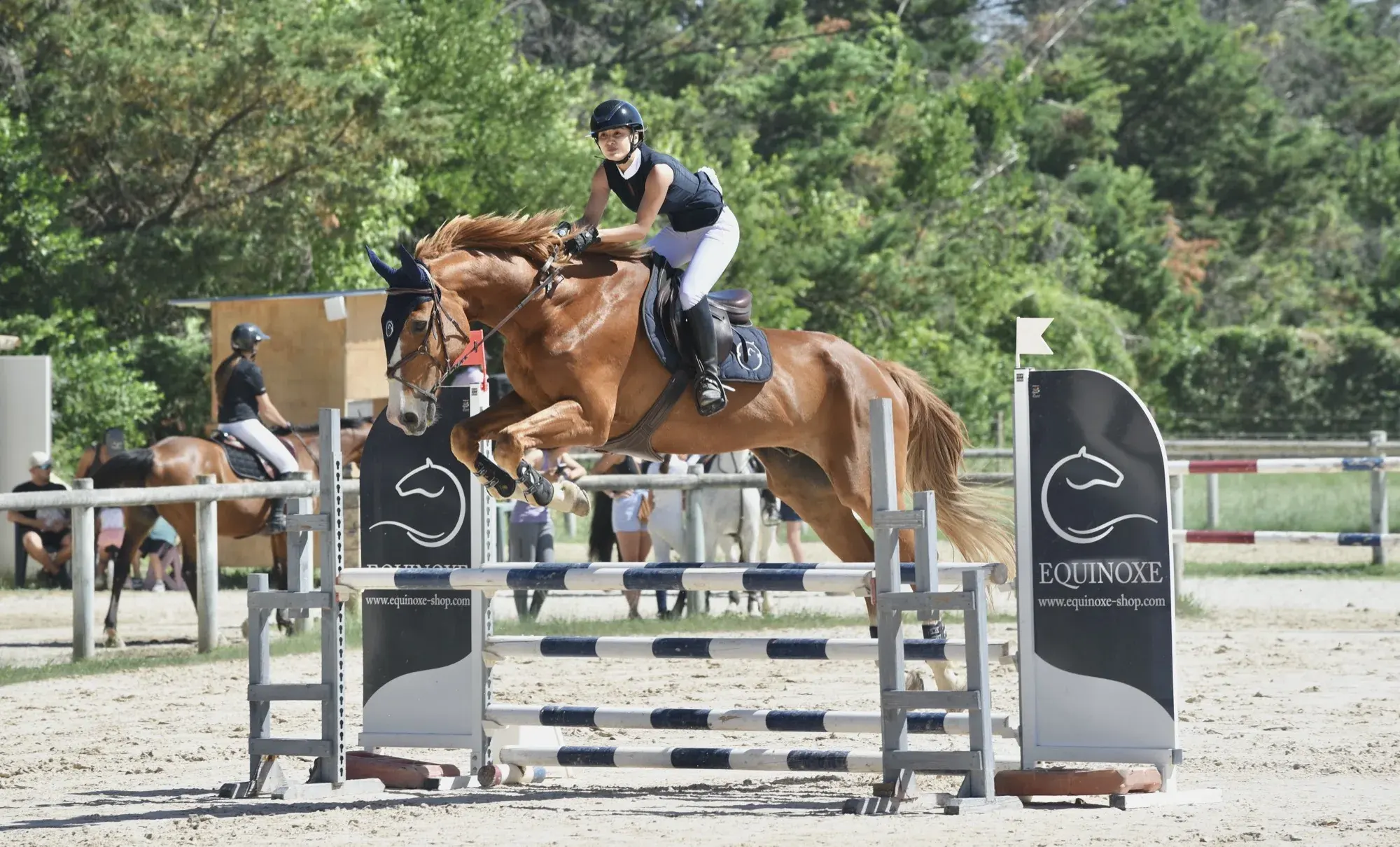 Saut d’obstacle en plein soleil, spectateurs en arrière-plan