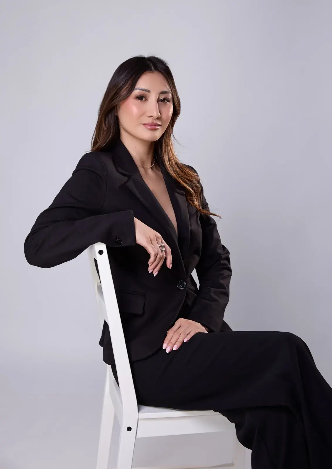 Assise en tailleur noir sur une chaise blanche, sourire léger, studio