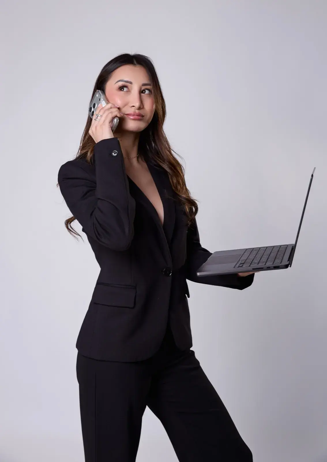 En tailleur noir, téléphone à l’oreille et ordinateur portable en main