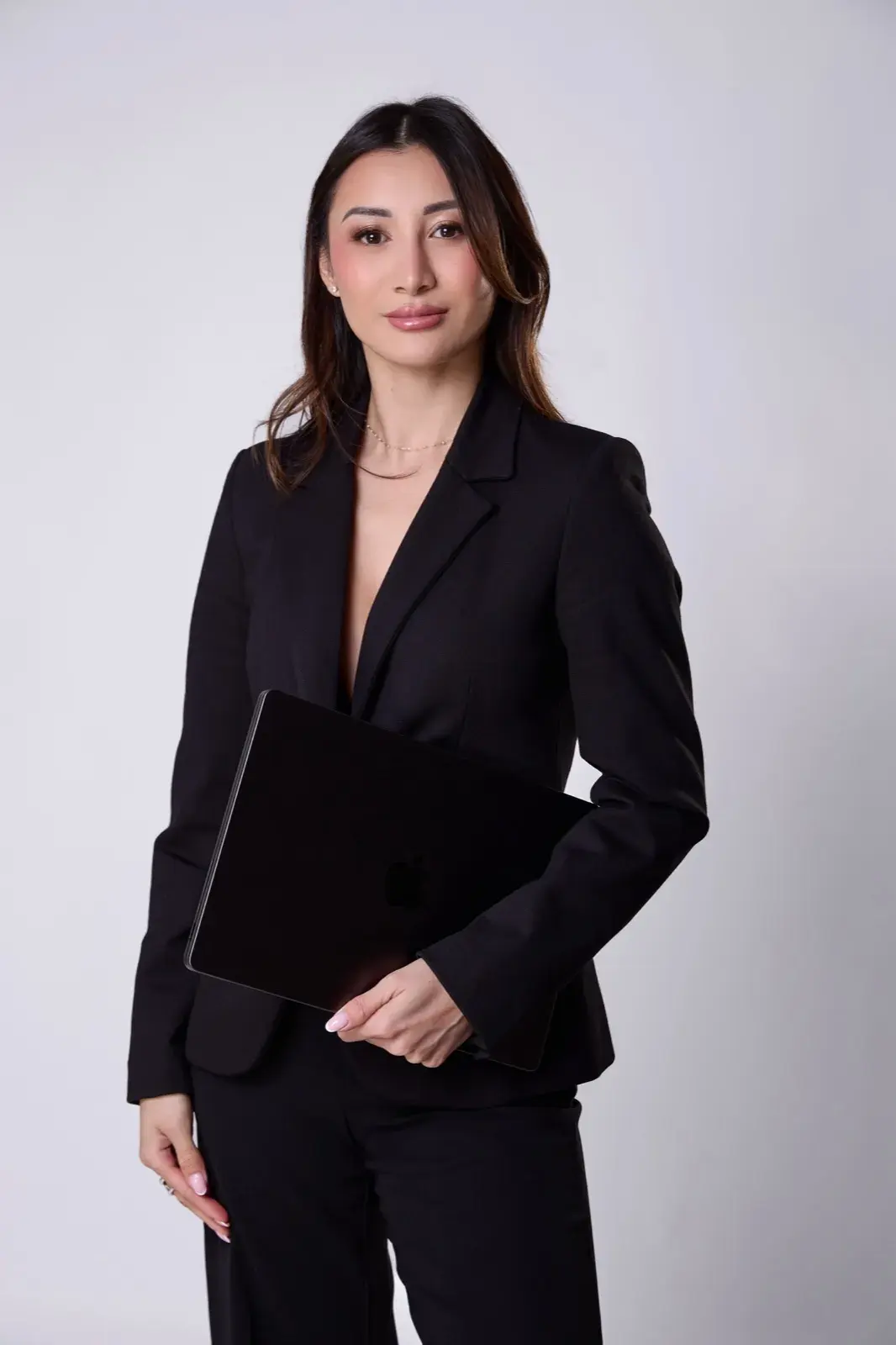 Face caméra en tailleur noir, ordinateur portable sous le bras