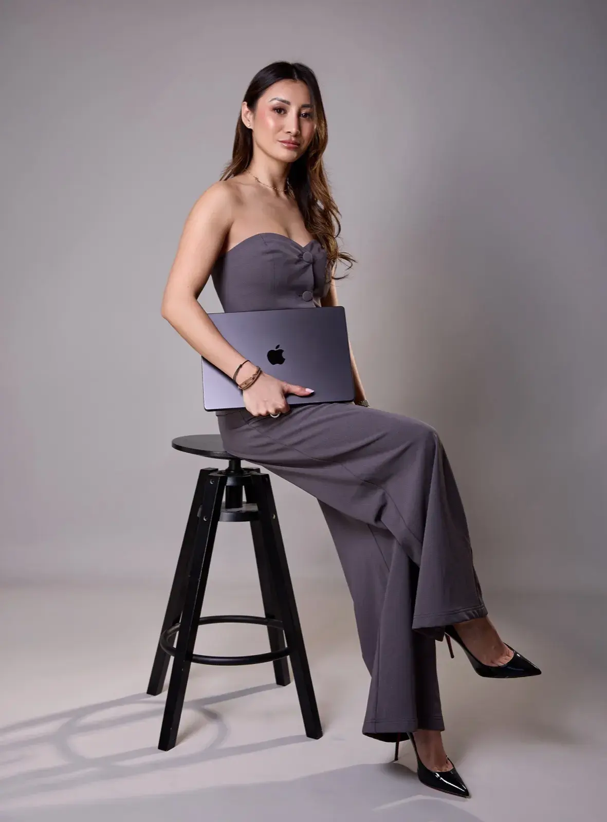 En combinaison bustier grise sur un tabouret, ordinateur portable contre elle