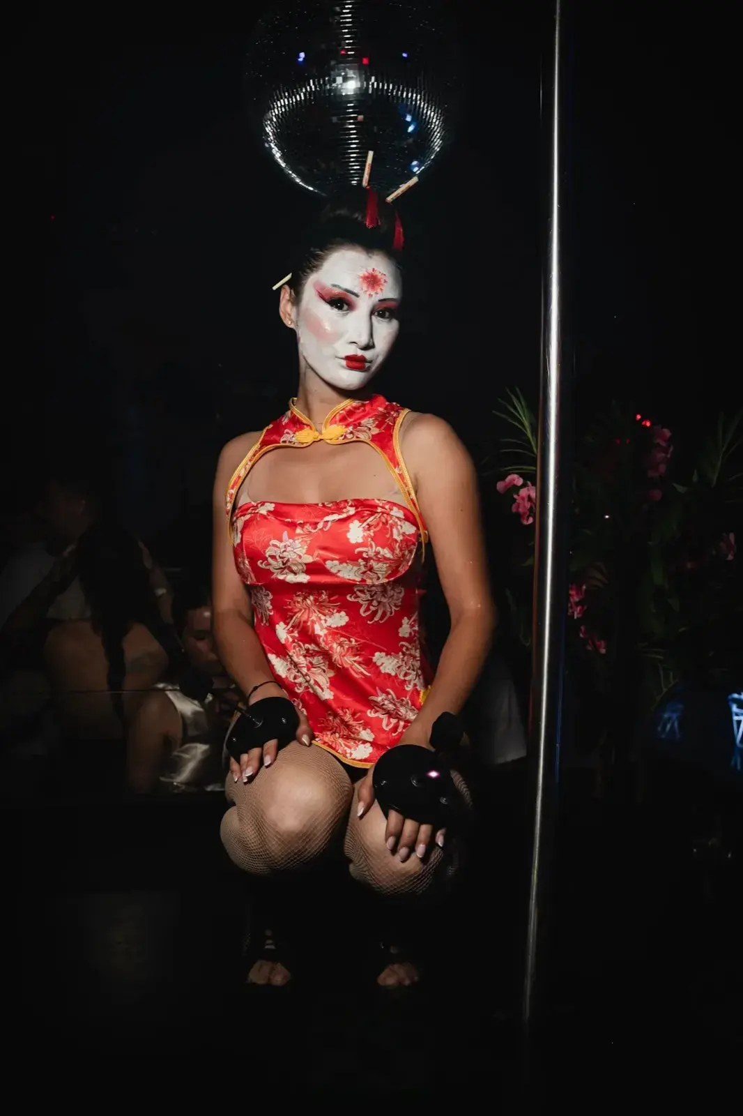 Accroupie devant la barre sous la boule à facettes, robe qipao fleurie