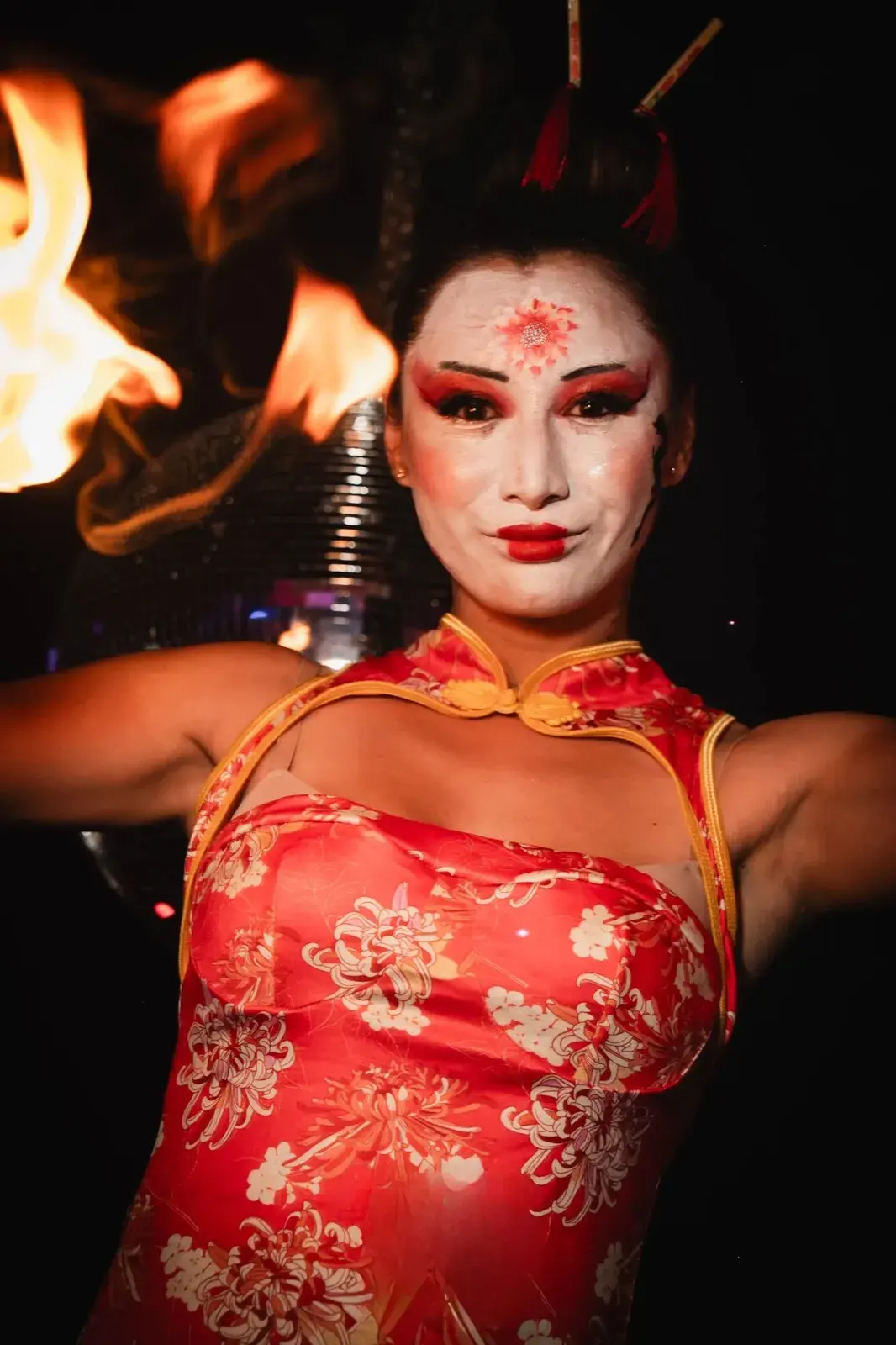 Buste face caméra, robe qipao rouge fleurie, flammes en arrière-plan