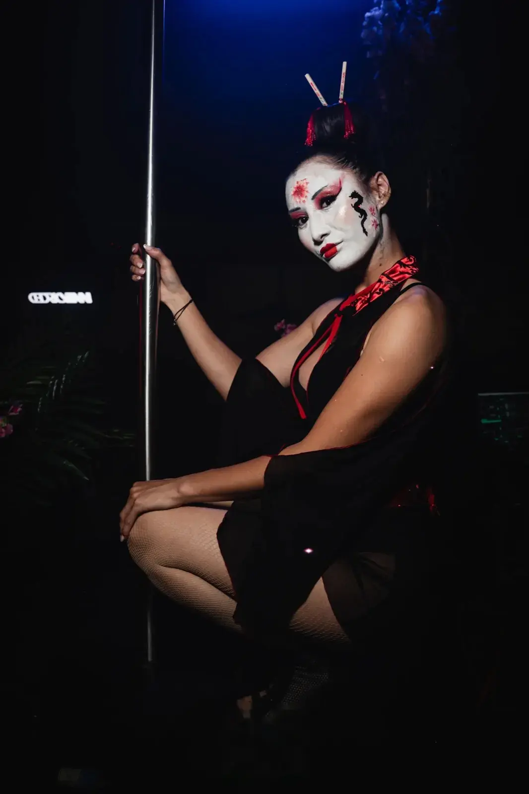 En pied accroupie près de la barre, tenue noire à col rouge satiné