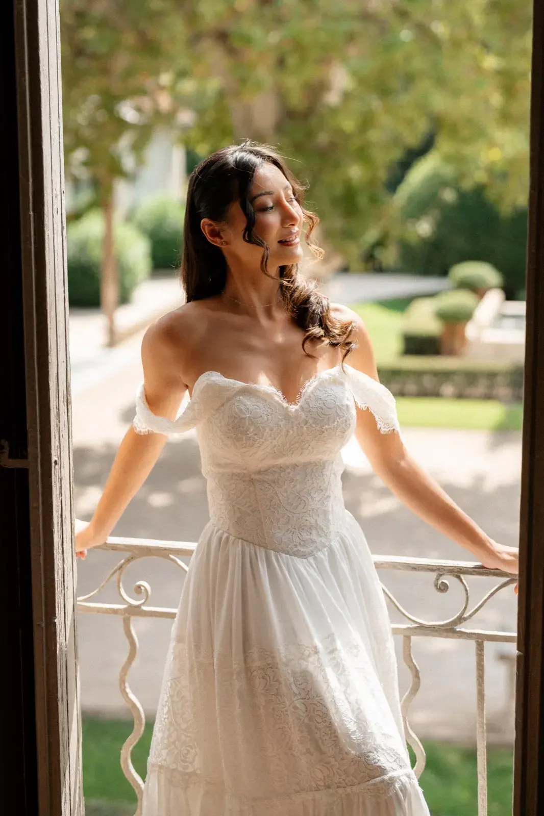 En mariée au portail, bras levé, paupières closes au soleil