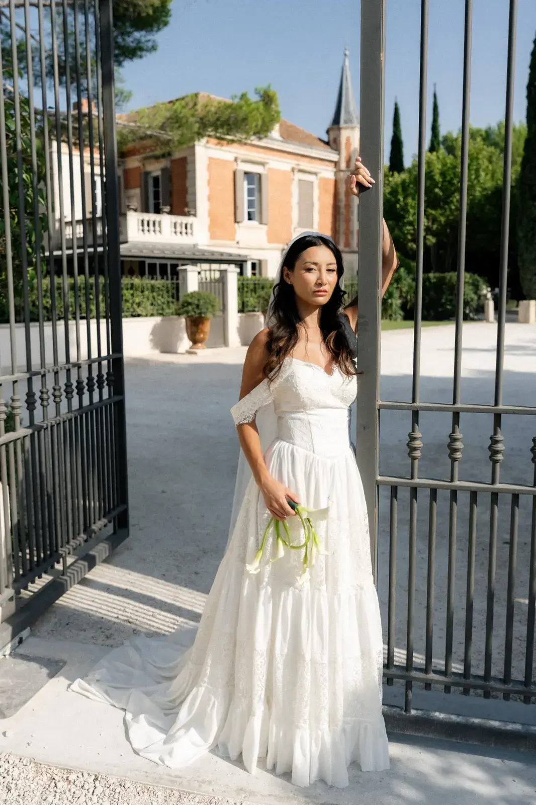 En pied au portail, robe de mariée et bouquet à la main