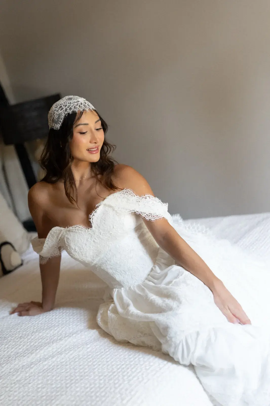 Assise sur le lit, robe à épaules dénudées, sourire doux