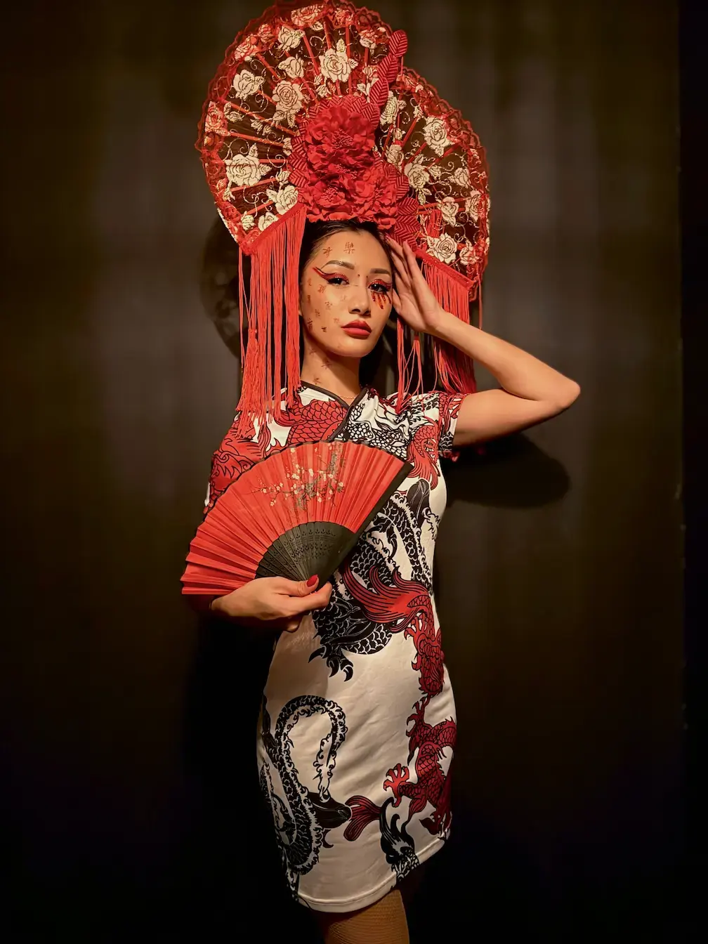 Plan américain, robe qipao blanche à dragons, coiffe rouge, éventail