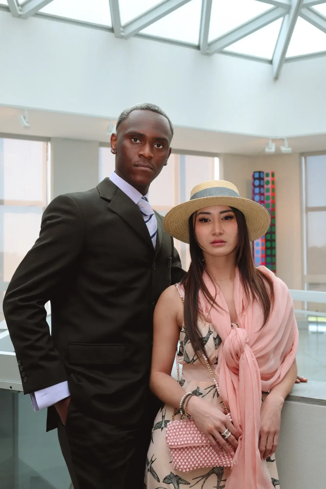 Portrait en duo, canotier et étole rose, aux côtés d’un mannequin en costume
