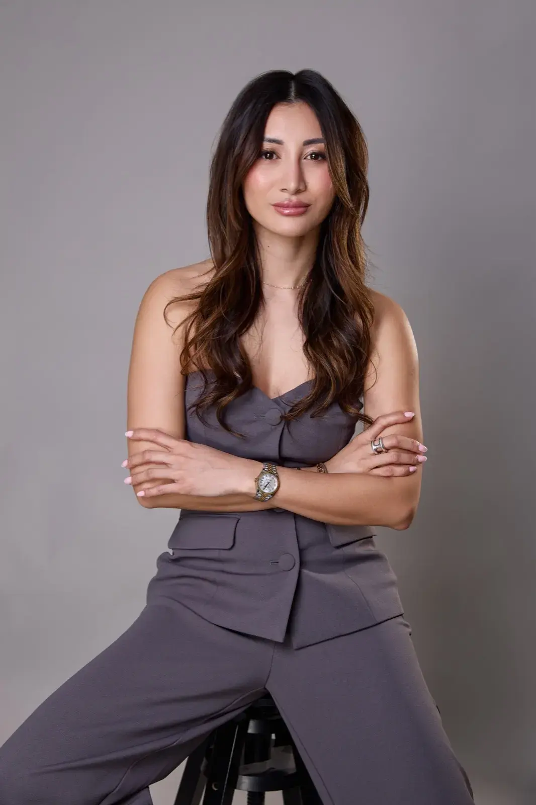 Assise sur un tabouret en tailleur bustier gris, bras croisés, regard direct